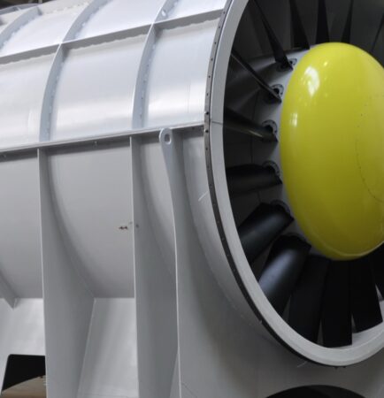 Industrial tube-axial ventilation fan with aerofoil blades and yellow nose cone in a factory