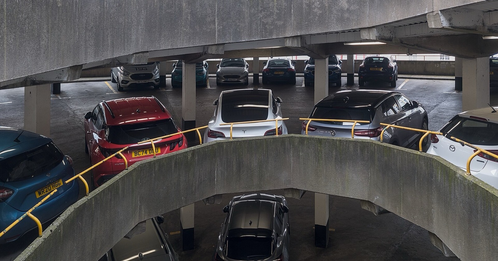 Interior of an enclosed multi-storey car park with parked cars, concrete decks and a spiral ramp